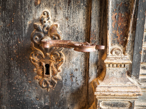 Antique iron door handle with ornate keyhole plate on a weathered wooden door, showing patina and craftsmanship for heritage, restoration, locksmith, security and historic architecture themes.