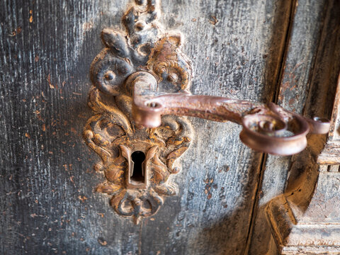Antique iron door handle with ornate keyhole plate on a weathered wooden door, showing patina and craftsmanship for heritage, restoration, locksmith, security and historic architecture themes.