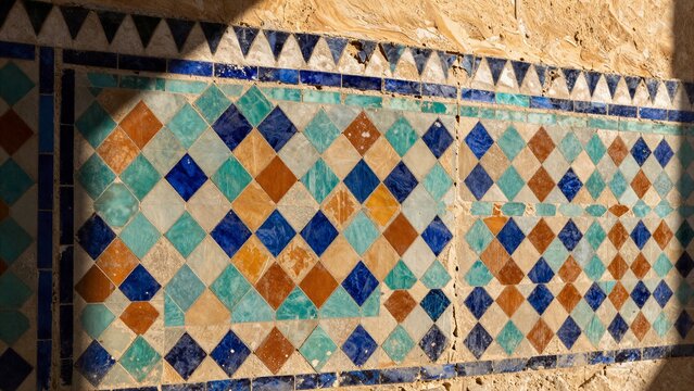 A close-up view of intricate Moroccan zellige tiles arranged in a geometric diamond pattern with vibrant blue, green and terracotta hues.