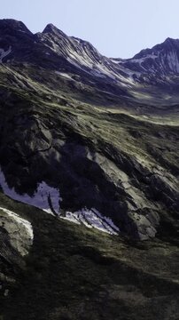 Towering mountains rise dramatically against a clear blue sky, their rocky surfaces adorned with patches of snow. Lush green valleys stretch out beneath, inviting exploration and awe.