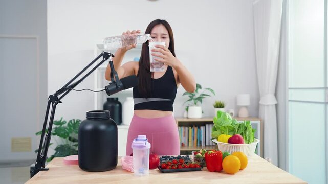 Young female vlogger making diet coaching video with fruits and blender in kitchen. Asian sporty woman streaming live tutorial about organic meals and holistic wellbeing.
