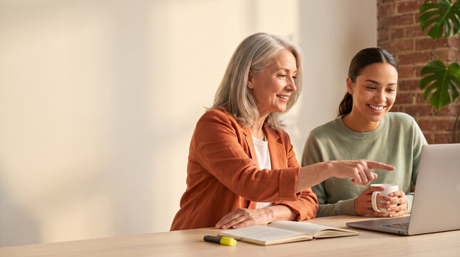 Senior businesswoman mentoring young female employee at office laptop, happy diverse colleagues working together on digital marketing strategy or corporate project website banner