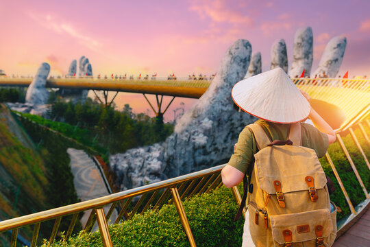 Tourist with straw hat and backpack admiring golden bridge at ba na hills, Da nang Vietnam