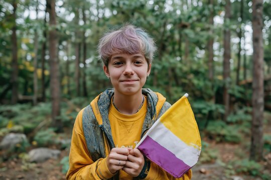 Young person with colorful hair holds nonbinary pride flag in forest