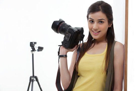 Beautiful young female holding camera against white background 