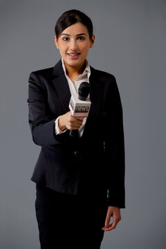 Portrait of woman news reporter holding out microphone against black background 