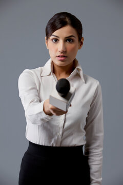 Portrait of serious reporter holding out microphone 
