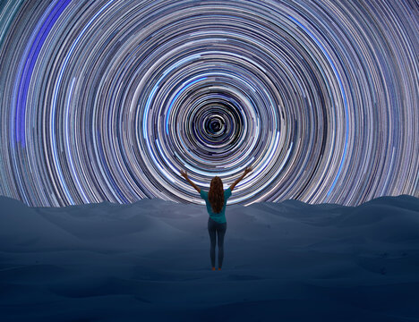 Woman overlooking a panoramic night sky with star trails and layered landscapes in desert