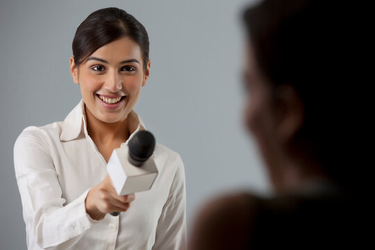 Smiling young female reporter taking interview of a person 