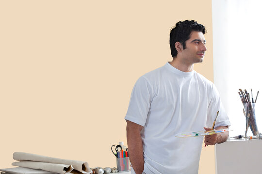 Young male artist holding paintbrush and palette 