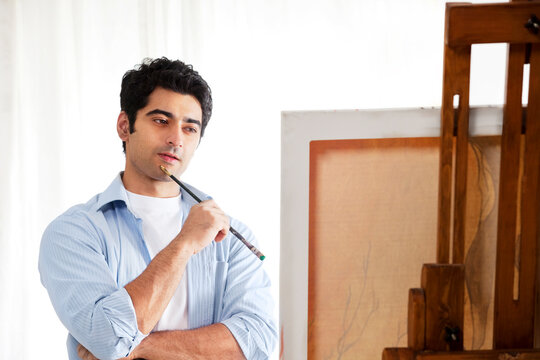 Thoughtful male painter standing in front of easel 