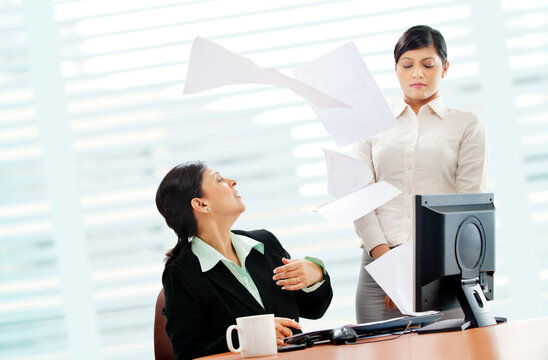 Furious mature businesswoman throwing papers on female executive 