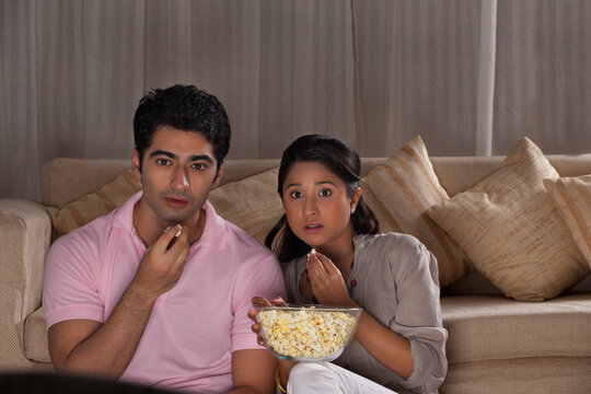 Young scared couple watching movie together at home 