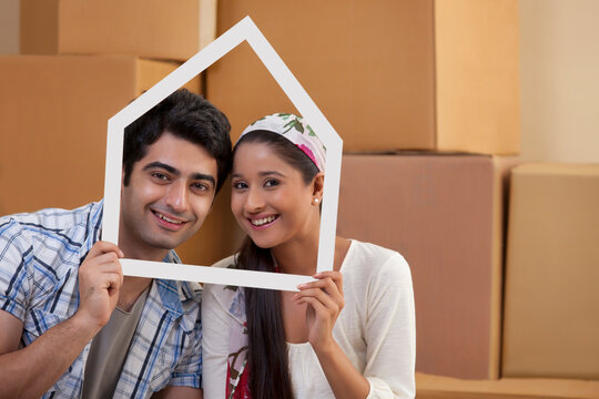 Portrait of smiling young couple looking through a house shaped frame 