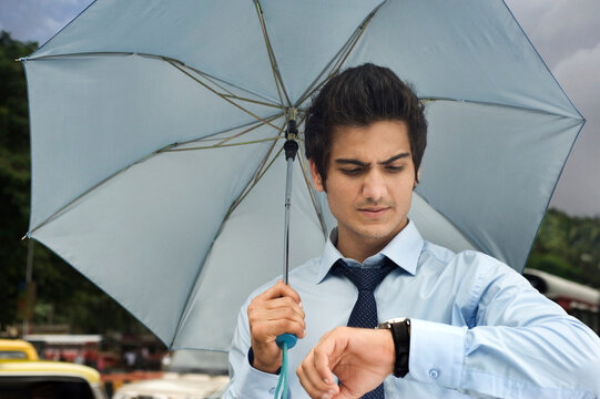 Businessman with an umbrella looking at his watch 