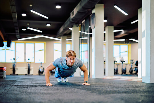 Athlete performing push-ups on gym floor, focusing on strength training and fitness development in a modern gym