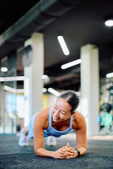Fotobehang Sportschool Woman performing a plank exercise on the gym floor, smiling and maintaining a strong posture, focusing on her fitness goals  © we.bond.creations