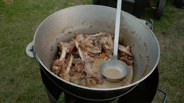 A kettle sits on the stove filled with meat, bones, and vegetables during a street food festival in Bukovina. People gather to enjoy the local flavors.
