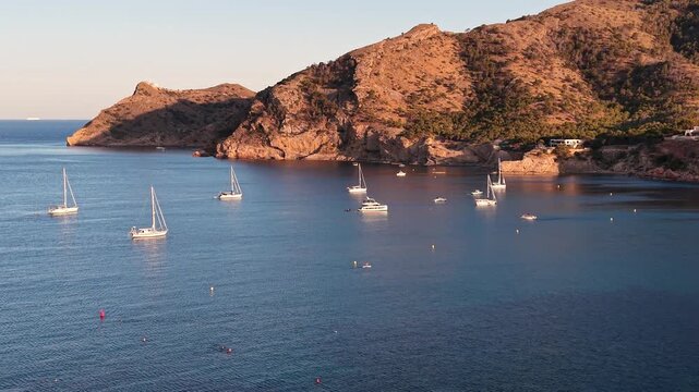 Aerial view of sailboats anchored in the calm blue waters of a bay near the rocky coastline of Altea, Valencian Community, Spain.