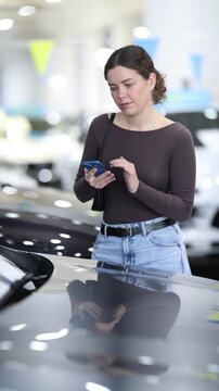 Young woman uses her smartphone to scan QR code on sticker on car window at car dealership