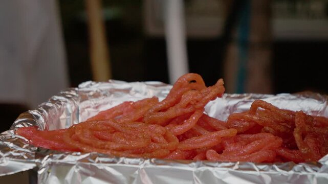 Street vendors preparing red jalebi in India. It captures the busy atmosphere during a festival, highlighting the popular dessert's preparation.