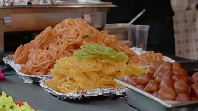 A vendor prepares colorful jalebi at a busy street food stall during a vibrant festival. People gather around to enjoy this sweet treat.
