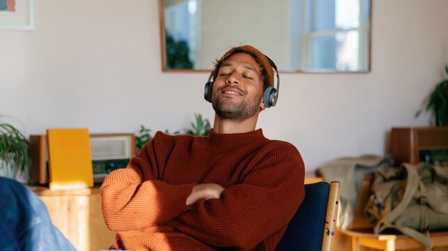 Man in a ribbed terracotta sweater wearing headphones with eyes closed, relaxing in a cozy vintage room for slow living and wellness concepts