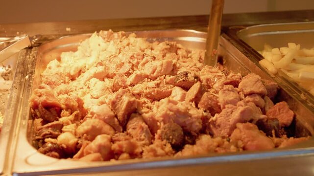 Meat is displayed in a stall window at a lively street food festival. Vendors serve people who enjoy various dishes made from fresh ingredients.
