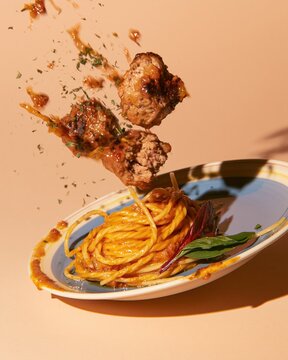 Meatballs falling through the air toward a plate of glossy spaghetti with herbs and basil, featuring hard shadows for food packaging and advertising