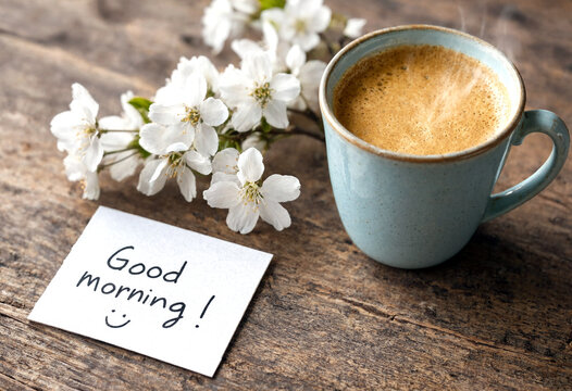 Freshly brewed coffee cup with a good morning note and delicate white flowers on rustic table