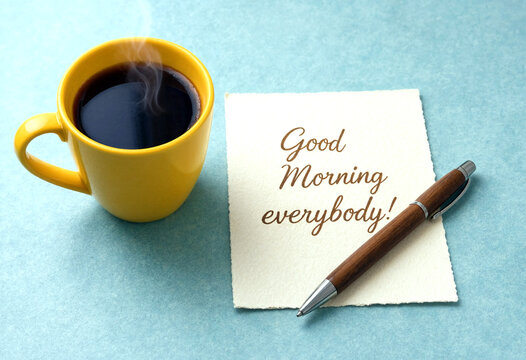 Yellow coffee cup with steam beside a good morning note and pen on blue background