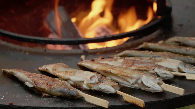 Trout cooks over an open fire at a street food festival. The aroma fills the air as people gather to enjoy fresh grilled fish cooked right in front of them.