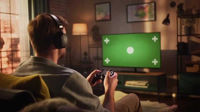 A man wearing headphones plays a video game on a large screen TV.