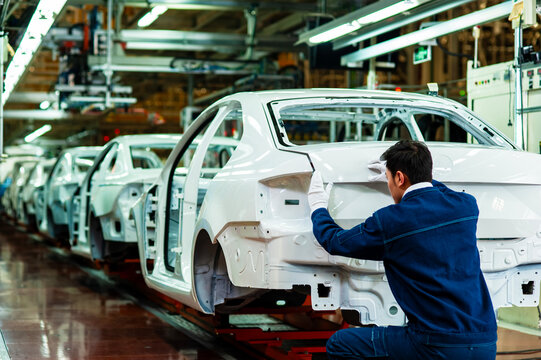 Workers at an automobile manufacturing plant inspect the body-in-white on an automated production line.
