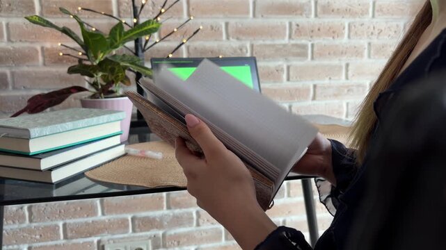 Woman working remotely from home holding a personal notebook, business person browsing a daily planner with a green screen laptop on a desk in the background