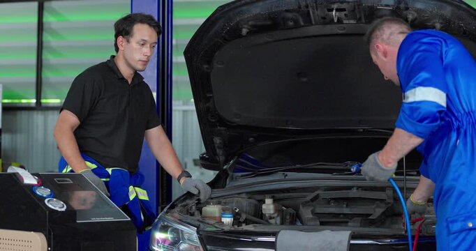 Auto mechanics servicing electric car air conditioning system with refrigerant recharge machine