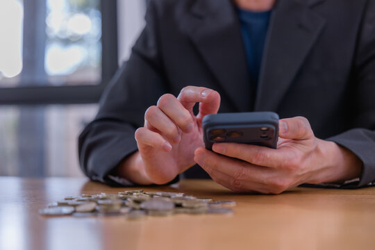 Business professional using smartphone with coins on desk, representing mobile banking, digital finance investment savings financial planning fintech technology and money management.