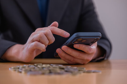 Business professional using smartphone with coins on desk, representing mobile banking, digital finance investment savings financial planning fintech technology and money management.