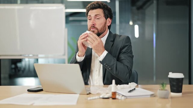 Businessman suffering from cold symptoms at office desk. Nasal congestion, sneezing, and headache indicate illness. Work continues despite feeling unwell, showing dedication amidst sickness.