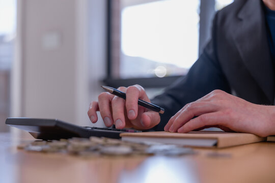 Business professional reviewing financial documents and writing accounting records with coins on desk, representing bookkeeping, budgeting, expense management, audit and financial planning.