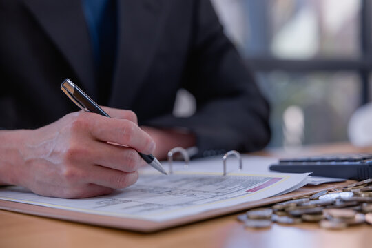 Business professional reviewing financial documents and writing accounting records with coins on desk, representing bookkeeping, budgeting, expense management, audit and financial planning.