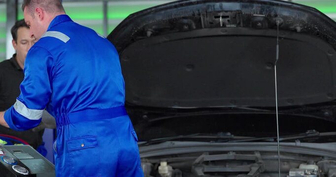 Auto mechanics servicing electric car air conditioning system with refrigerant recharge machine