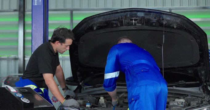 Auto mechanics servicing electric car air conditioning system with refrigerant recharge machine