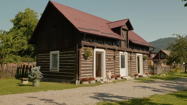 A boy walks into a traditional house located in the Bucovina region. The house has wooden walls and a red roof, showing local culture and architecture.