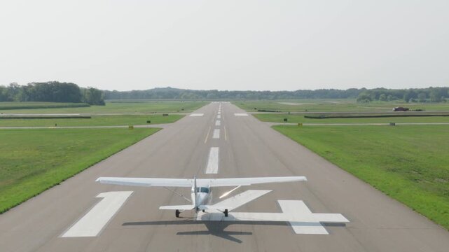 Small single engine airplane accelerates down empty runway and climbs into hazy sky above green countryside on calm summer morning