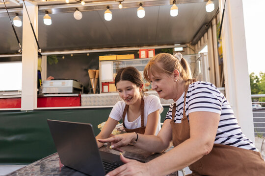 Women entrepreneurs planning business strategy on laptop outside food truck