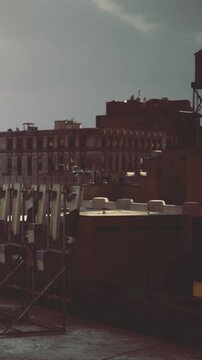 Sunlight spills across a bustling cityscape, highlighting rooftops and water towers. The scene showcases a blend of architecture and urban features, creating a tranquil moment.