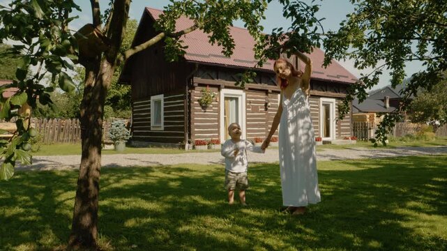 A woman and her young boy are walking in front of a traditional house in Bucovina. They enjoy their time outdoors under the warm sun on a clear day.