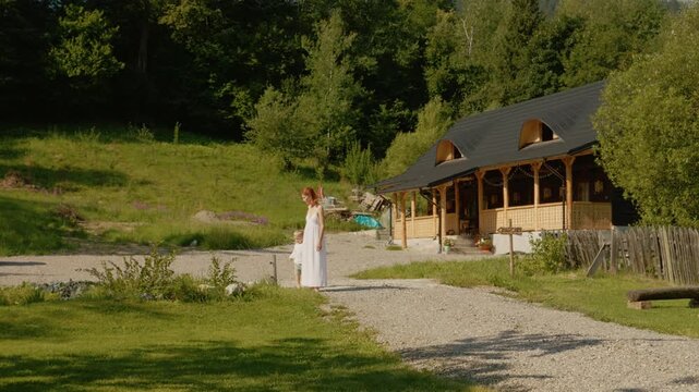 A woman and her boy are walking along a path near a traditional house in Bucovina. They enjoy the warm weather and the beauty of nature surrounding them.