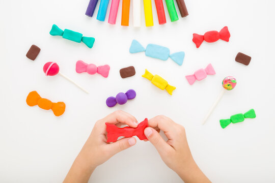 Little child hands making and creating colorful beautiful candy shapes from modeling clay on light gray table background. Closeup. Point of view shot. Flat lay. Top down view.